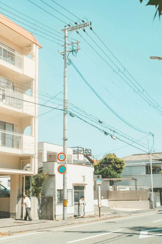 an empty city street corner with electric wires and two people walking across