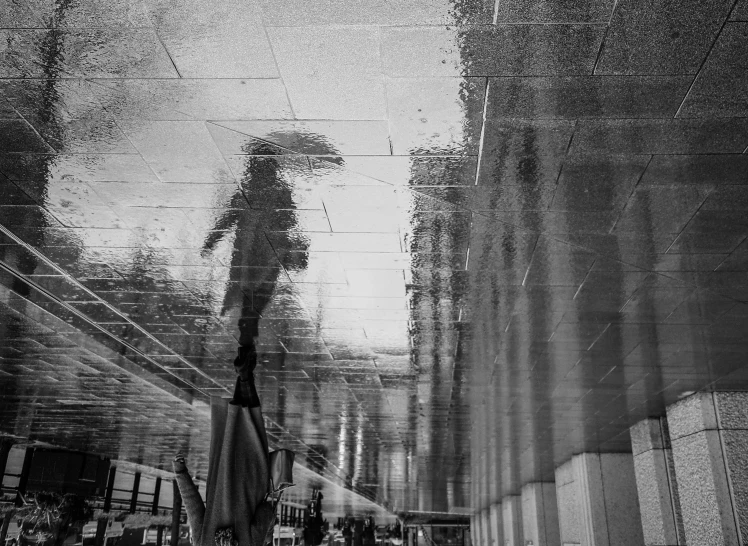 the reflection of an umbrella and a building on the wet pavement