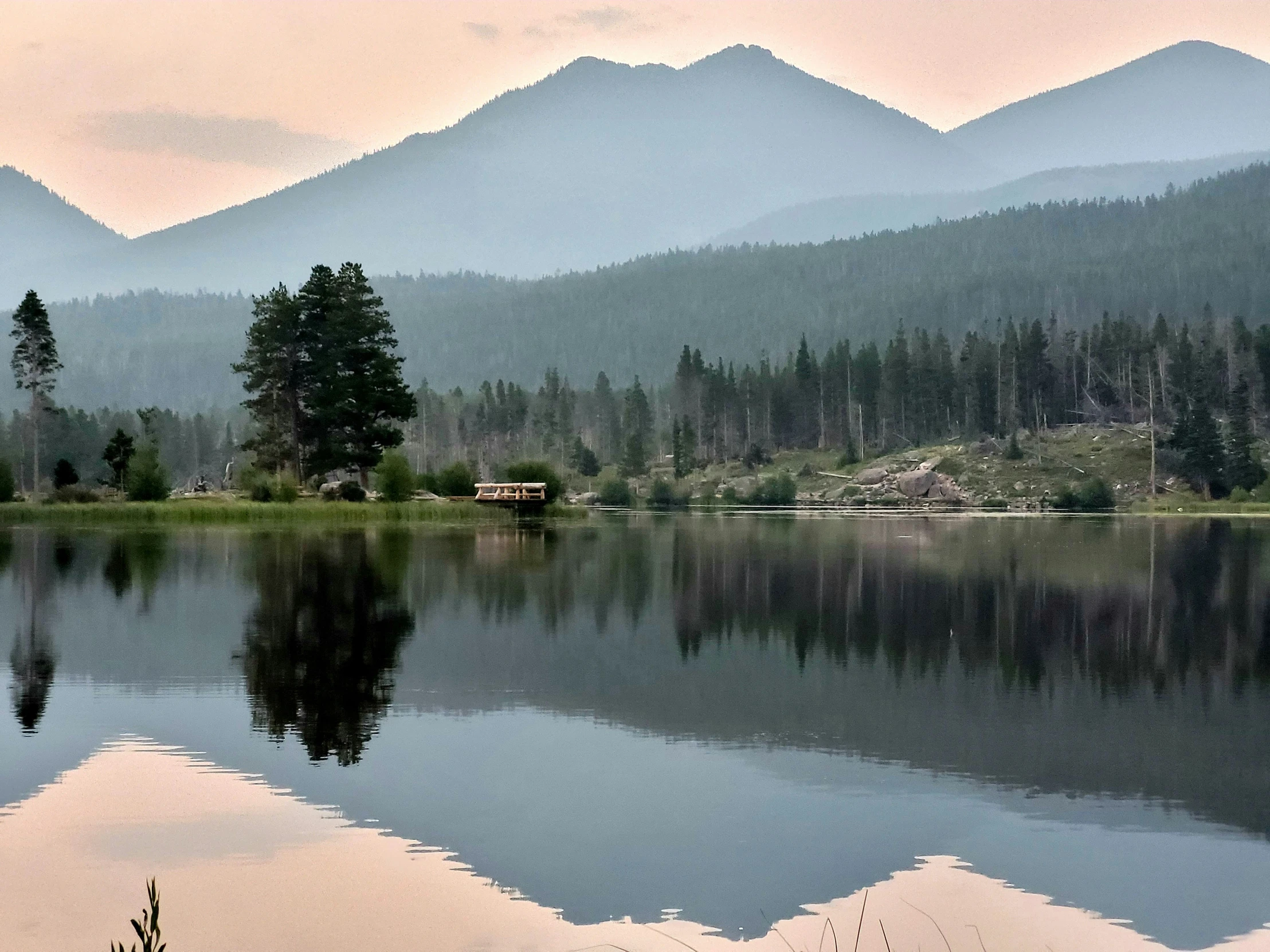 the water with several trees around it and mountains behind it