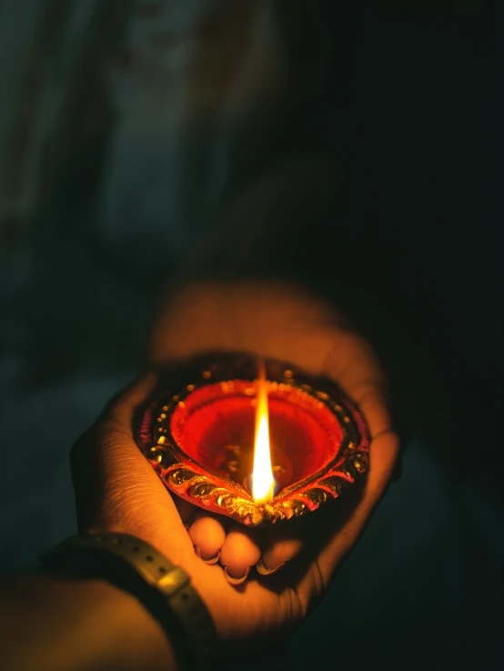 a woman's hands hold a small diya, a candle in the middle