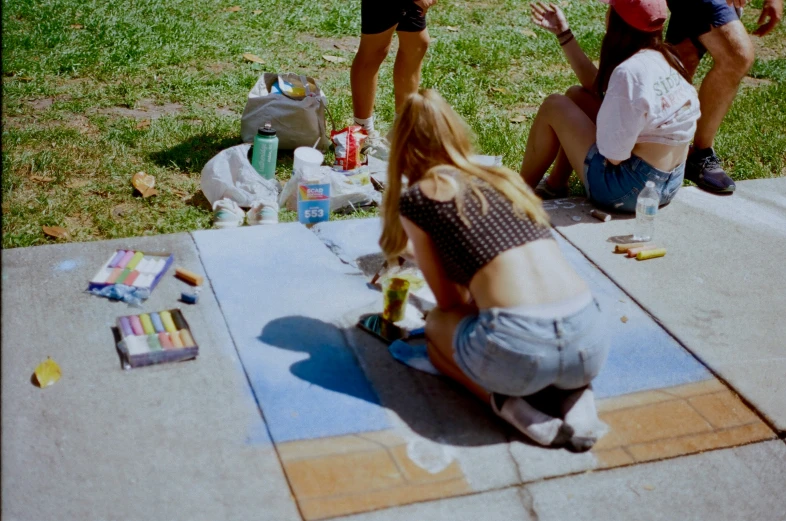 three people sit at a sidewalk in a park