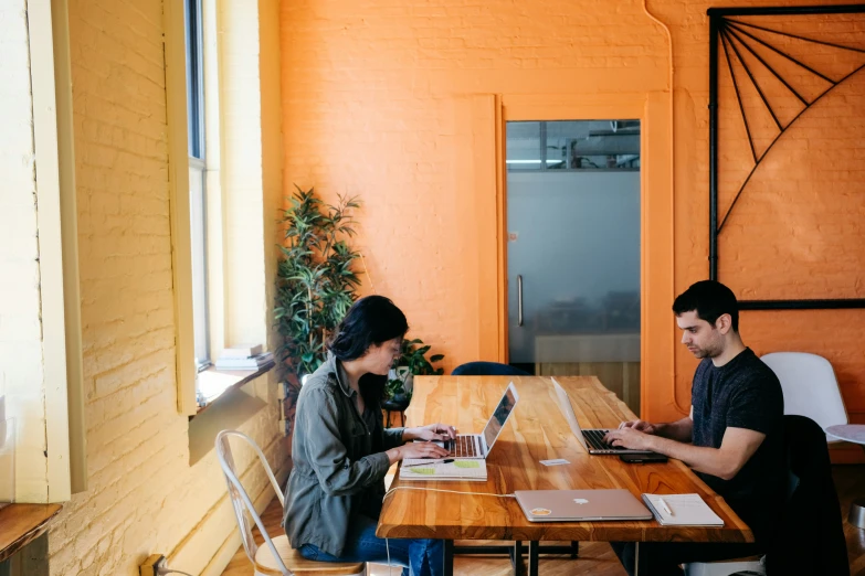 two people sit at a table near an open laptop