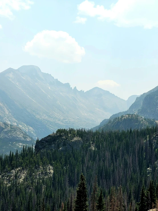 two people walking on a mountain side with tall mountains behind them