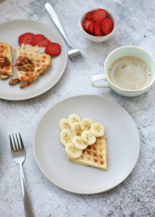 a plate topped with banana slices next to a bowl of strawberries and a cup of coffee