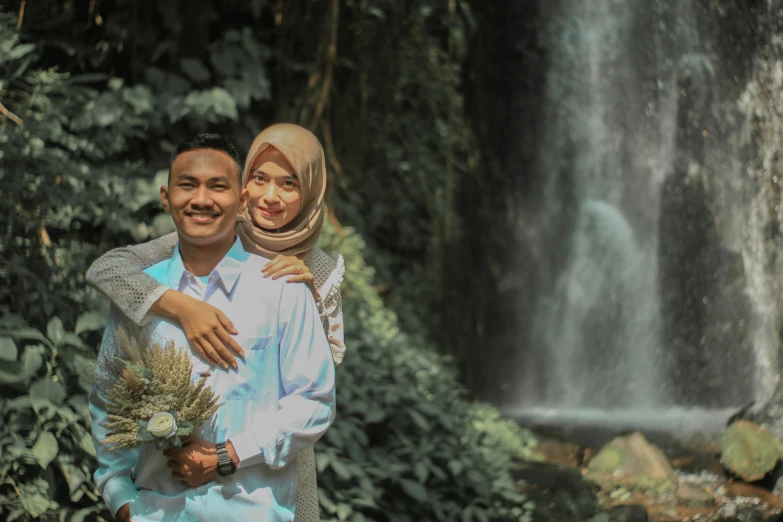 two people holding a flower in front of a waterfall