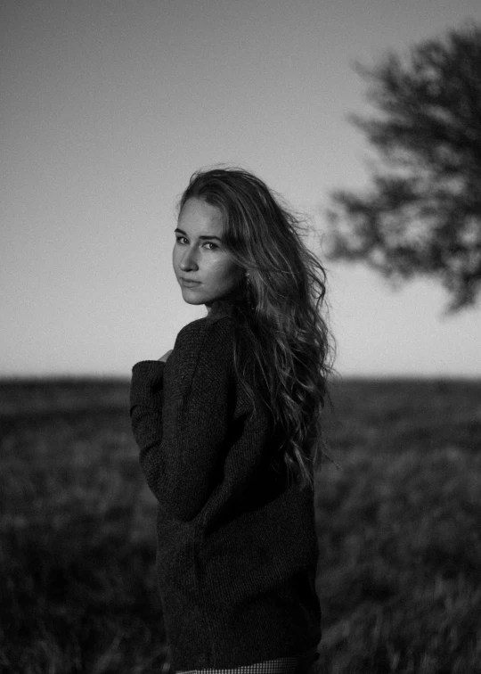 a woman in black standing on grass with her arms behind her head