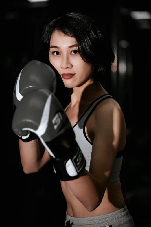 a woman with black hair posing for a po while holding a boxing glove