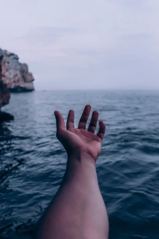 a hand extending out above the water with a cliff in the background