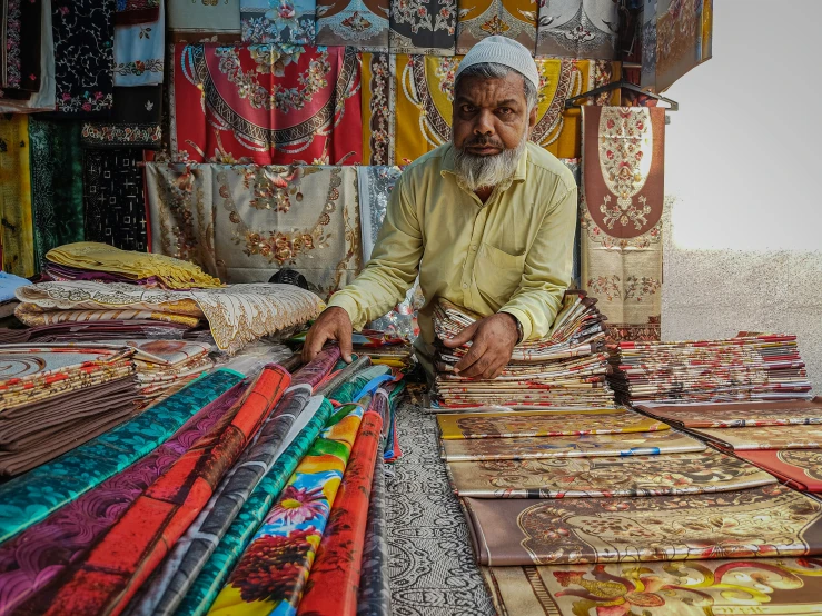 a man kneeling down next to a bunch of colored fabrics