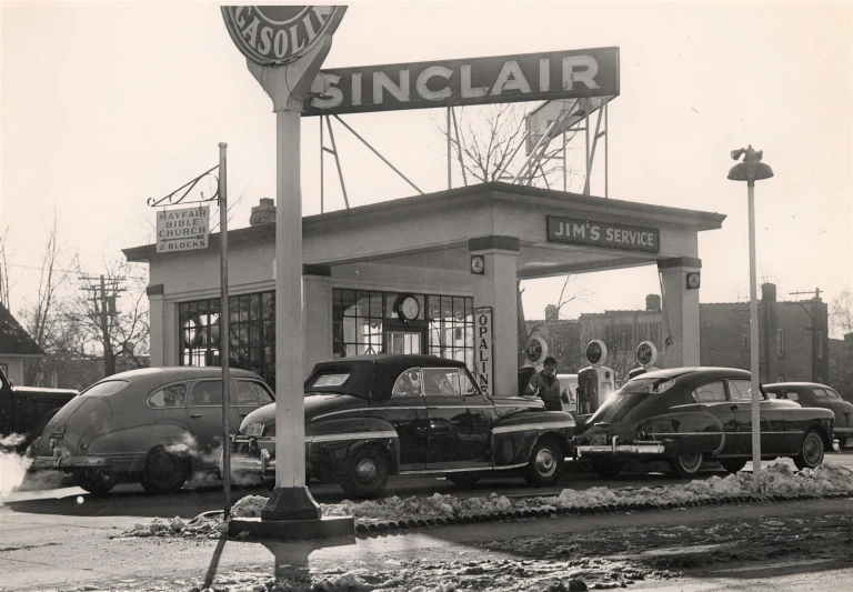 a black and white image of a gas station with cars lined up in front