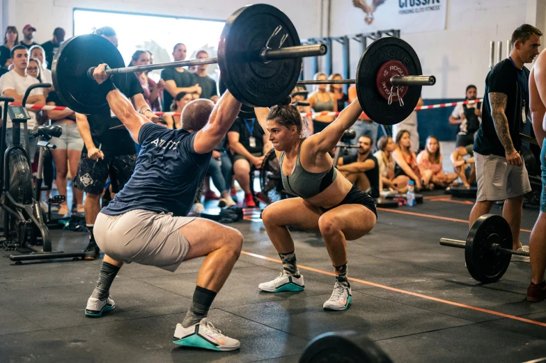 a man and a woman are performing an overhead squat in a gym