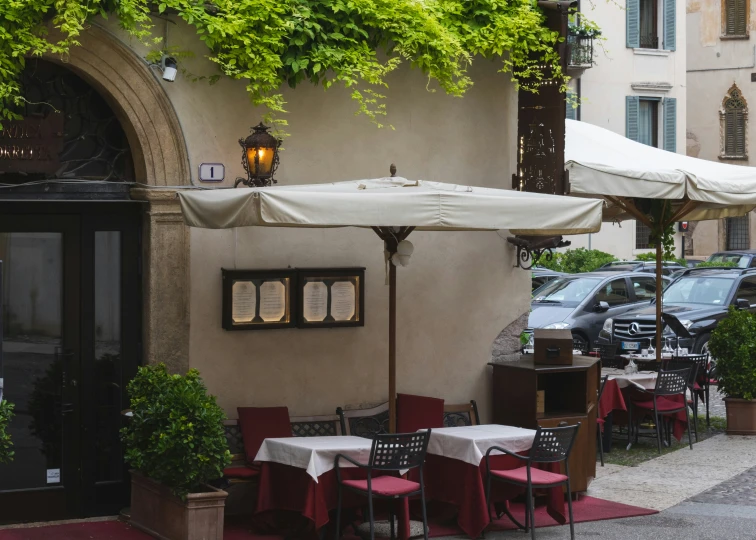 tables with chairs and umbrellas line the outside of an old building