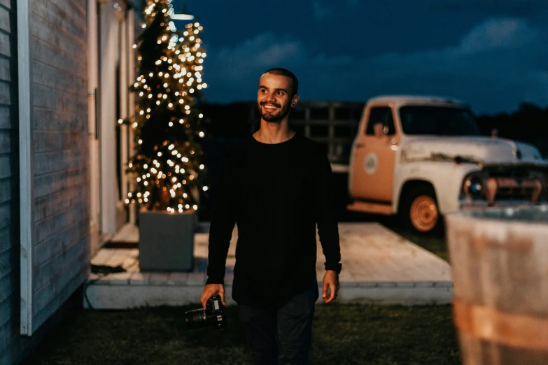 a man in a black shirt stands in front of a lighted christmas tree