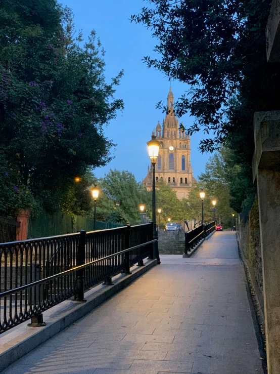 a narrow sidewalk leads to a large stone building at twilight