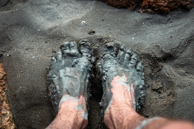 a man's feet sticking out of the ground on a beach