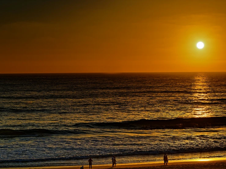 a sun set and two surfers walking on the beach