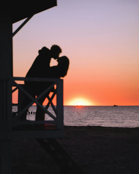 a man and woman kiss as the sun sets