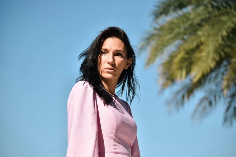 a young woman poses in pink dress with palm tree in background