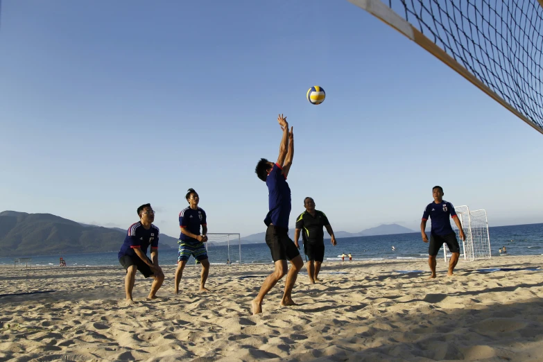 four people playing volleyball on the beach with the mountains behind them