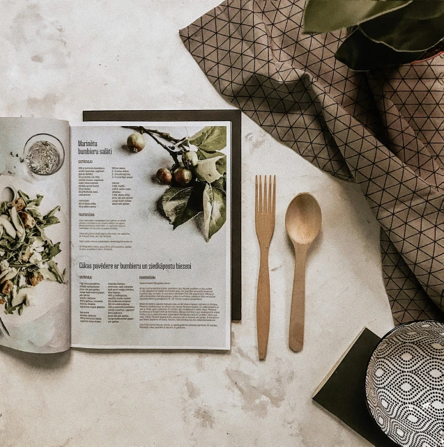 an open menu next to a teaspoon and spoon on a table