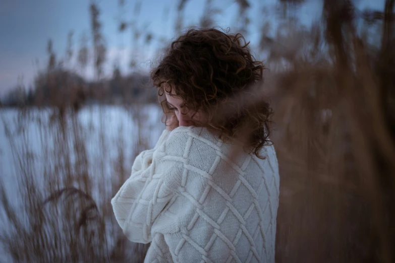 a woman in sweater standing near snow covered water