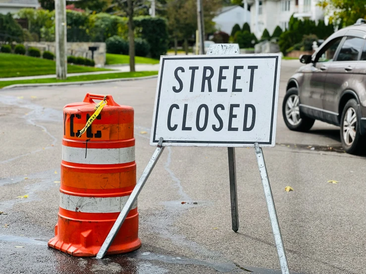 a street closed sign next to a traffic cone on the side of a road