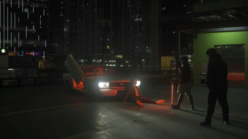 two people standing next to a red car in a dark city