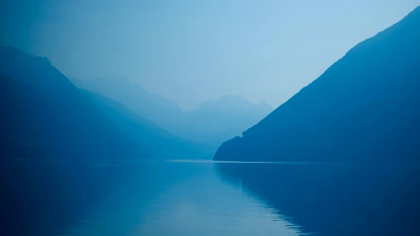 a river with the light coming on and its water reflecting the mountain tops