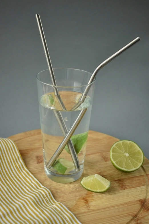 lime and two drinking straws in a glass of water with a small piece of lime next to it