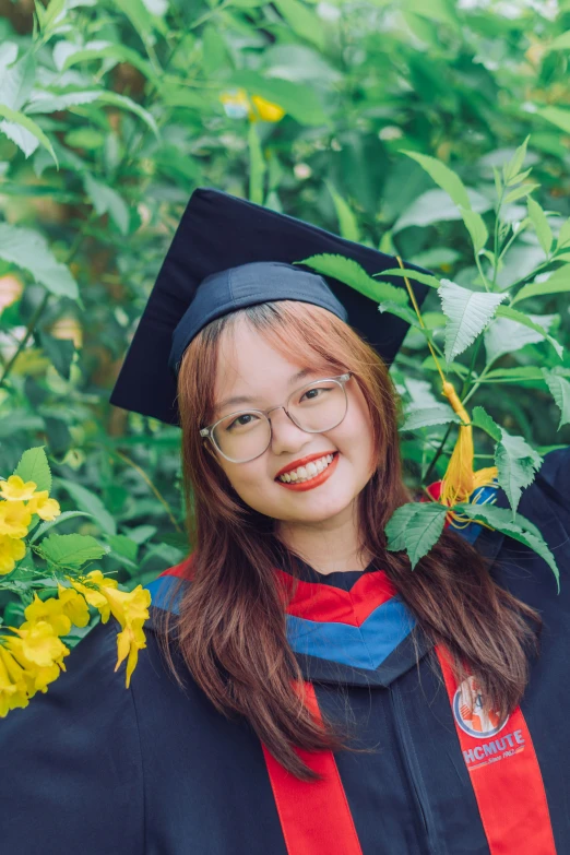 a girl with long hair in glasses, a red and blue striped dress and a black graduation cap smiles as she wears her graduation regal regal garb