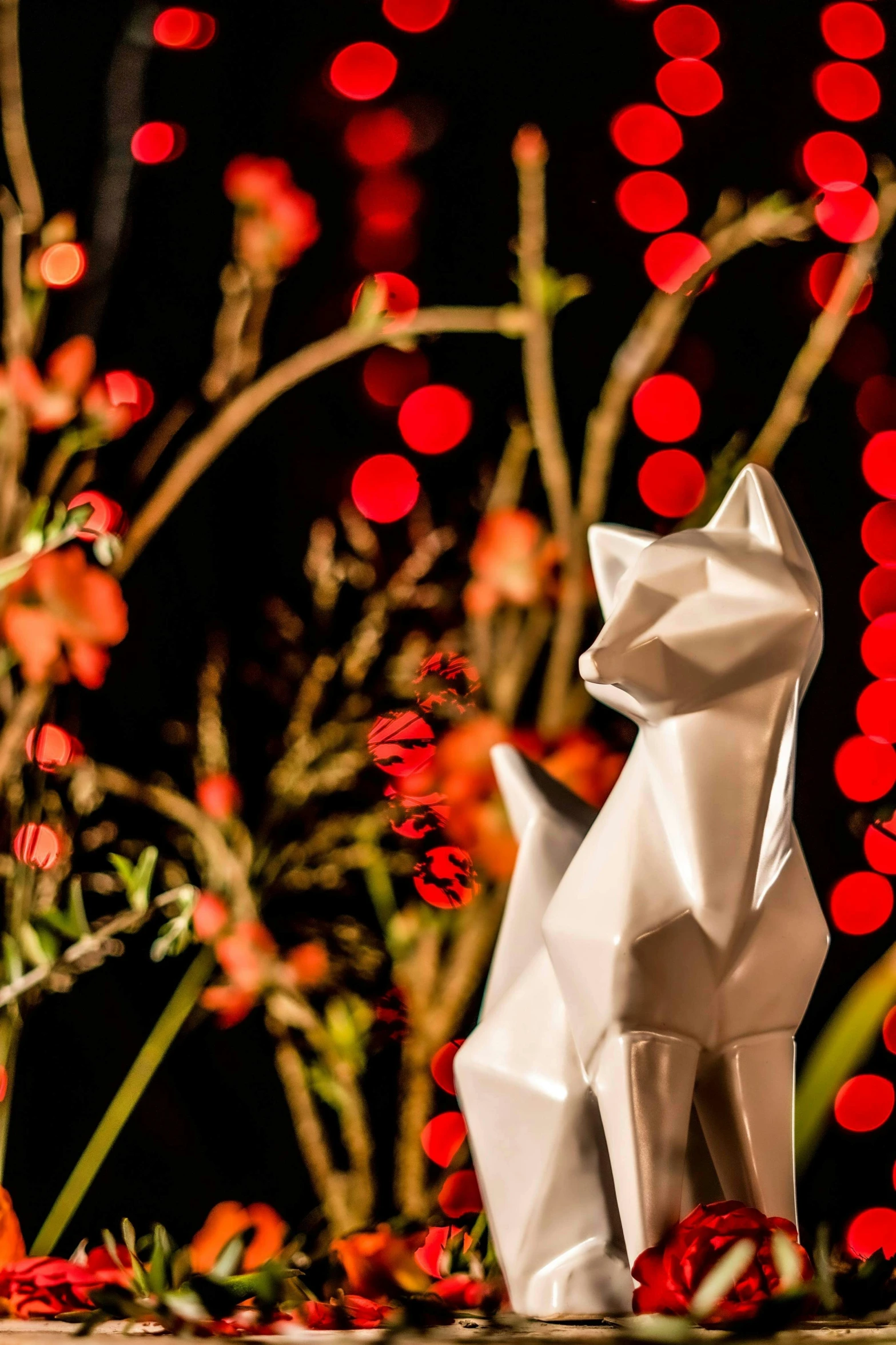 a white origami animal sits amongst flowers and blurry lights