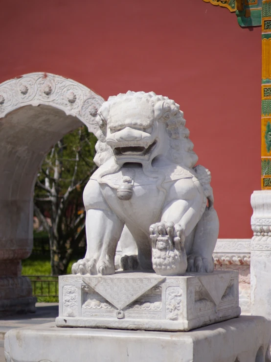 statue of lion sitting on small pedestal in outdoor setting