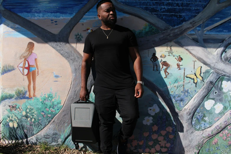 a black man holding a suitcase is standing in front of a mural