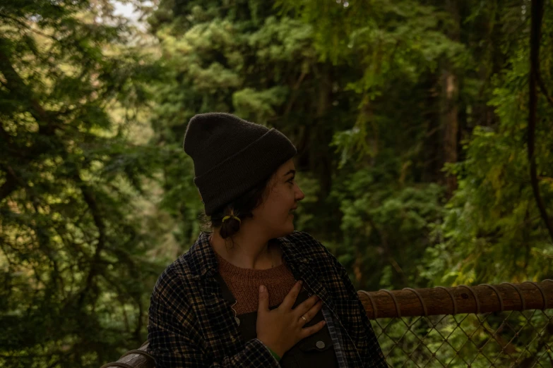 a woman in a hat is standing on a rail near trees