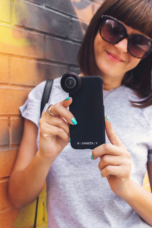 a woman holding a black phone while wearing sunglasses