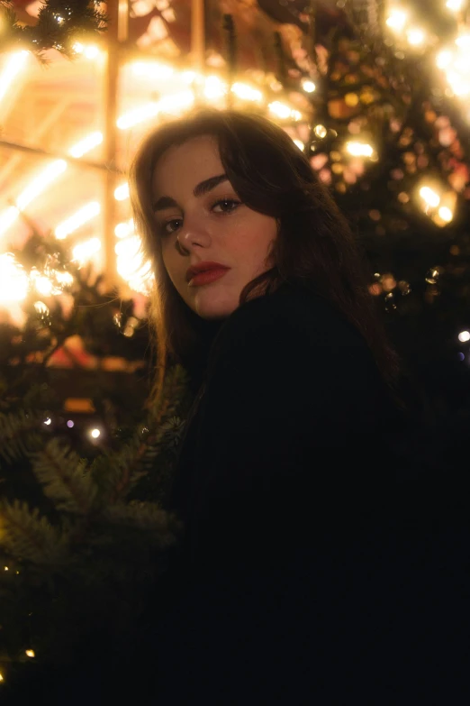 a woman standing by a christmas tree lit up in the dark