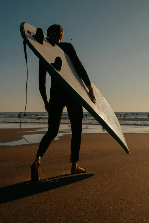 a man in black wetsuit holding a white surfboard