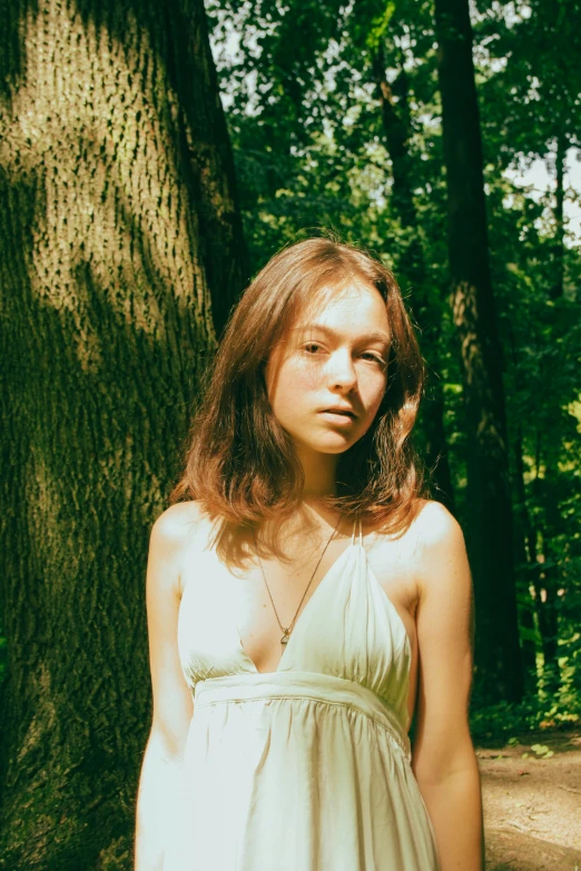 a pretty young lady in a white dress standing in the woods