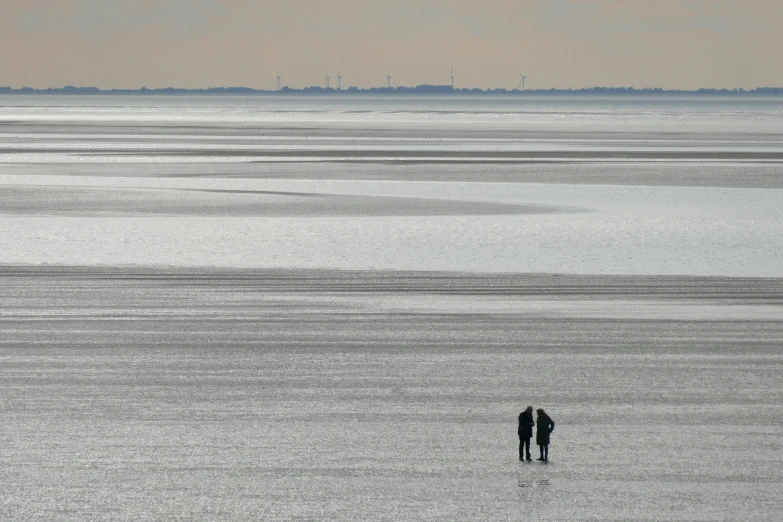 two people walking along the shore near some water