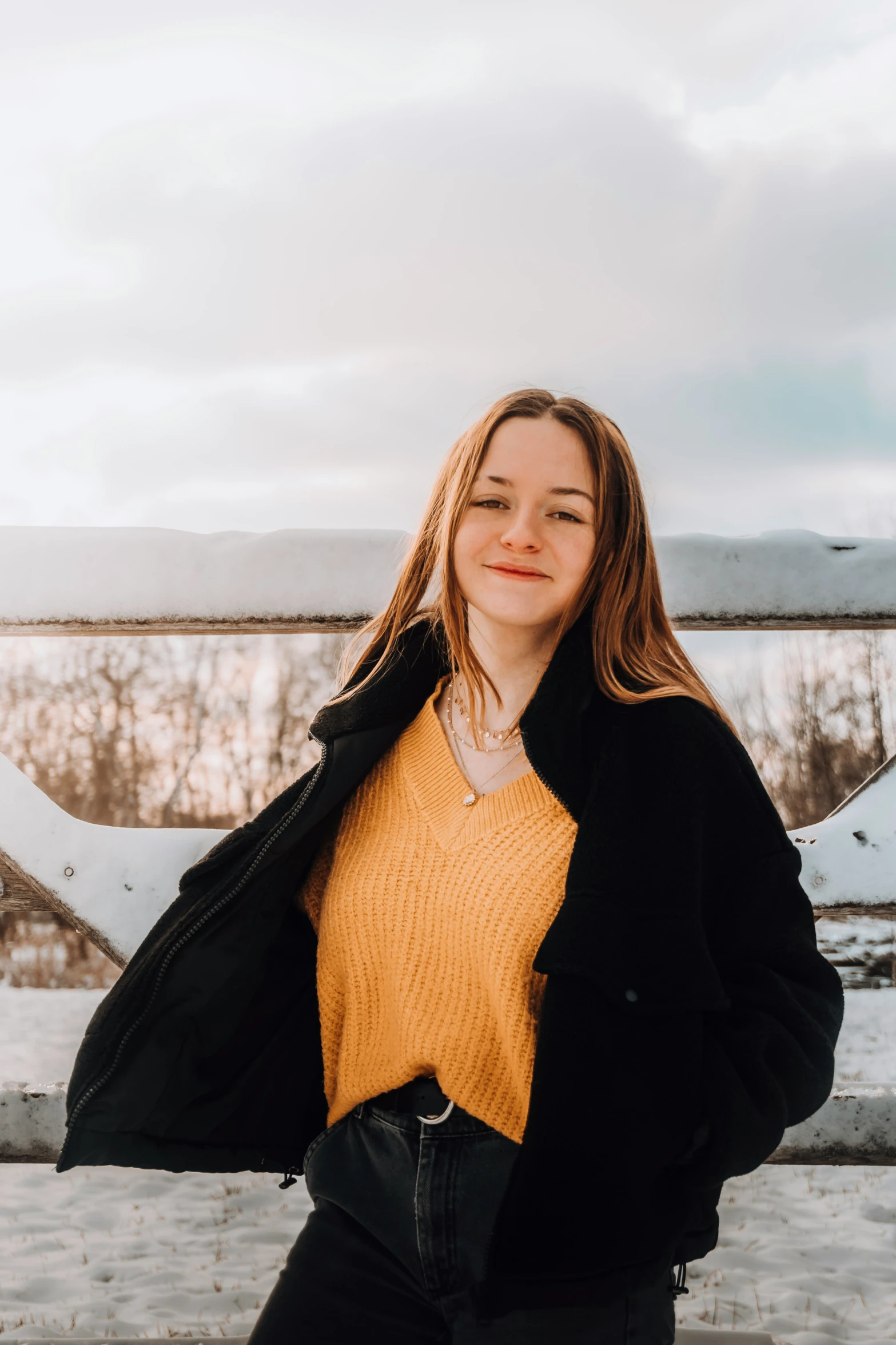 a young woman posing outside with snow and clouds in the background