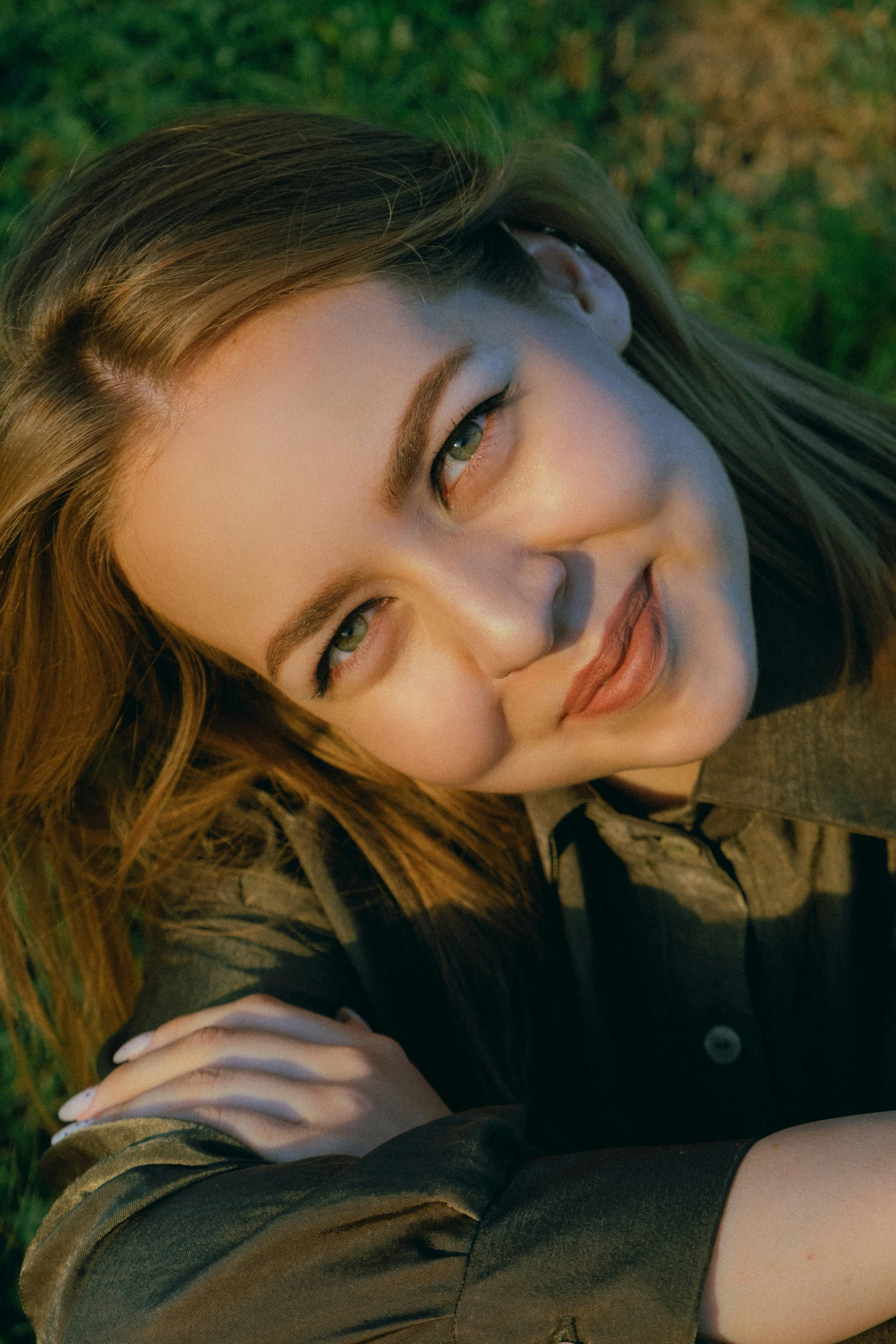 a girl laying down in the grass and looking at the camera