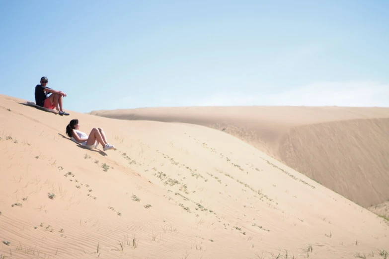 two people are sitting on a sand dune