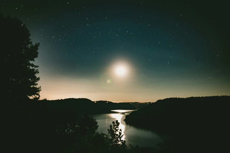 the moon shining over a body of water and a forest