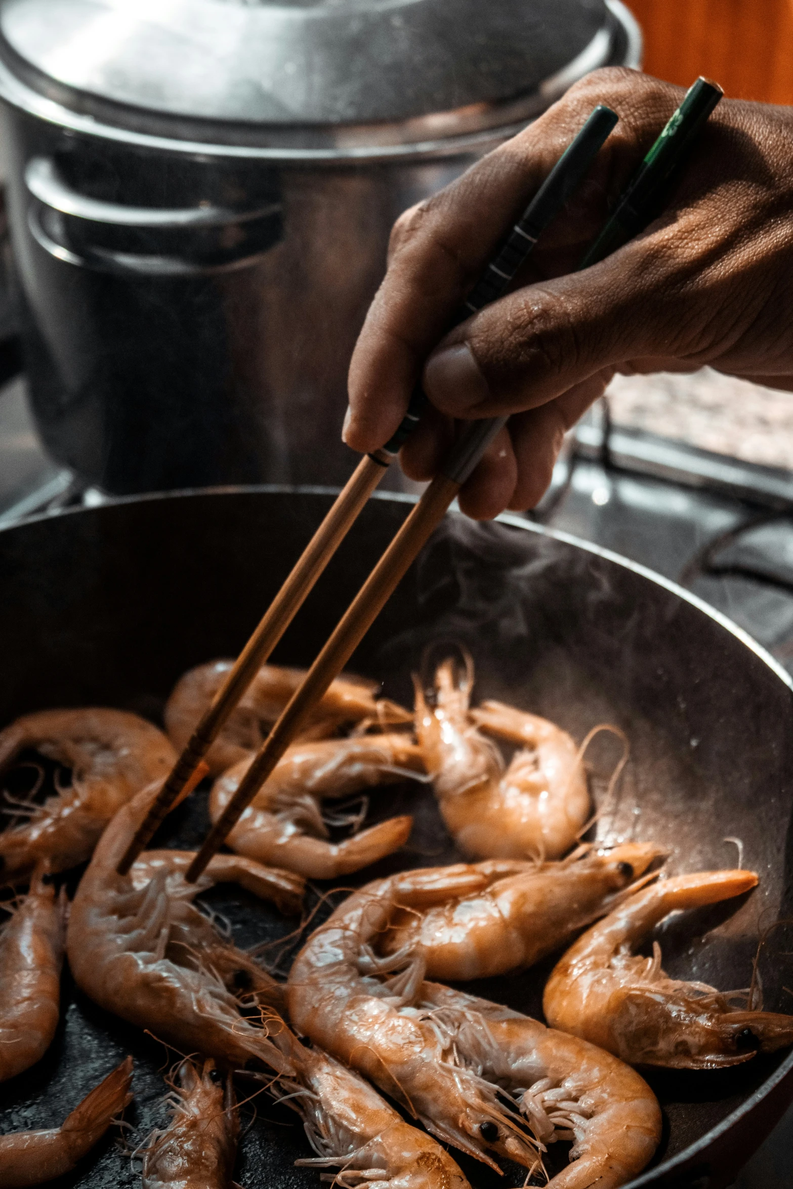 a person holding chopsticks over shrimp in a wok