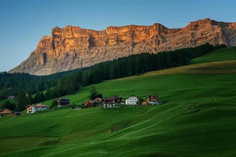 the mountain is next to the grassy field and there are cottages on it