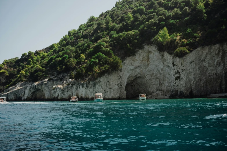 boats out at sea under green trees by a rock mountain