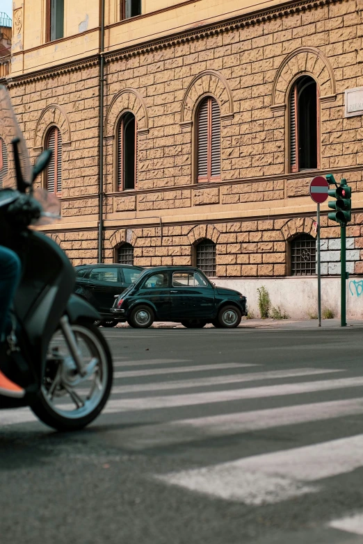 the moped rider is driving by a parked green car