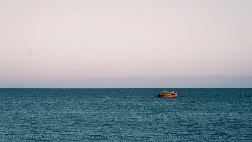 a small orange boat sailing in the middle of a blue sea