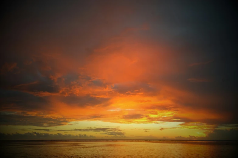 the sky is very orange with clouds and water