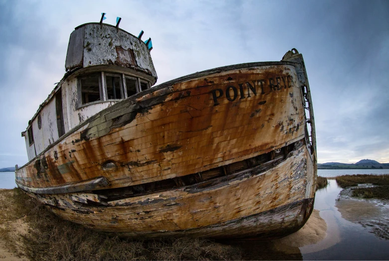 an old abandoned boat on the shore in front of the ocean